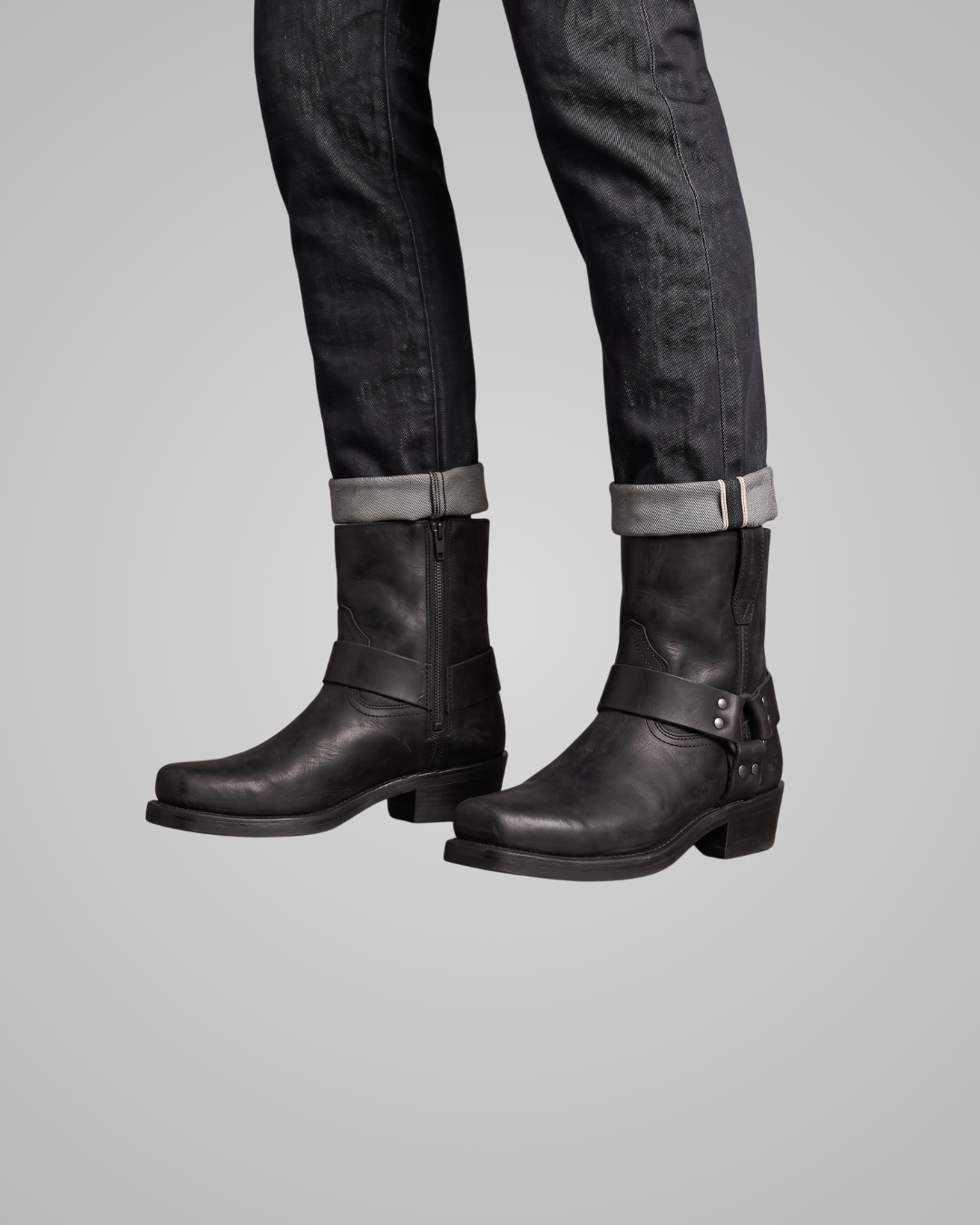 Black leather boots worn with black jeans on a gray background