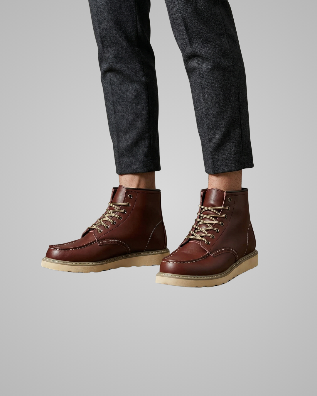 Brown leather boots worn with dark gray pants on a light gray background
