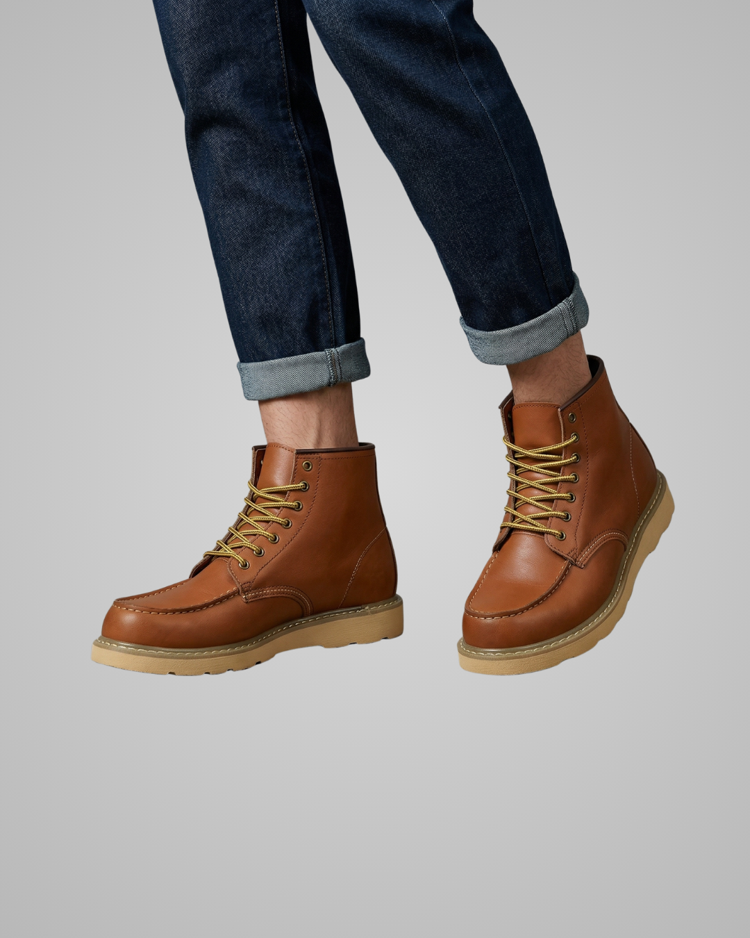 Brown leather boots worn with rolled-up jeans on a plain background