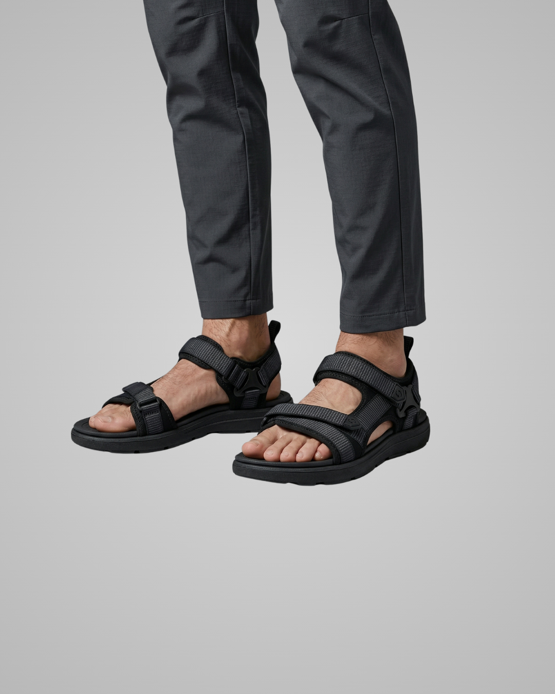 Person wearing black sandals and dark pants on a gray background
