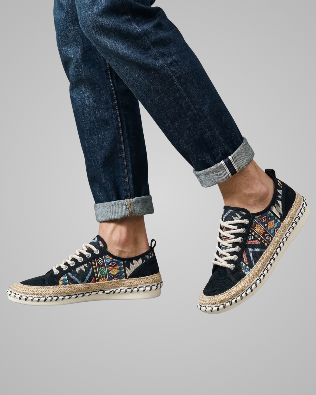 Navy espadrille shoes with patterned sole worn with rolled-up jeans on a gray background
