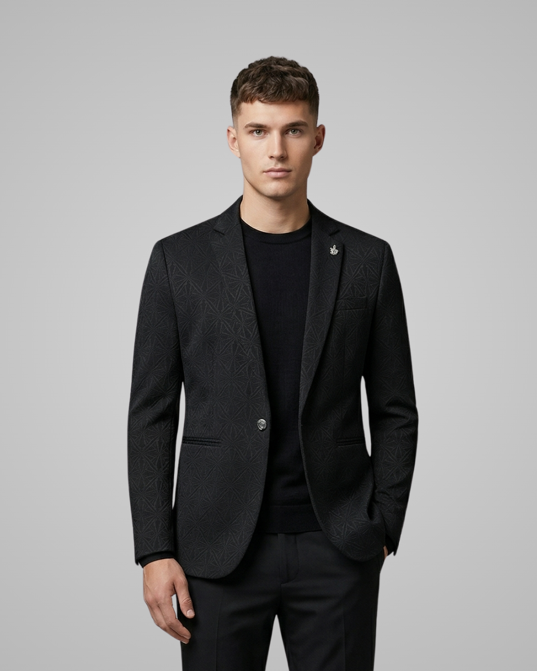 Man wearing a black suit jacket over a black shirt on a gray background