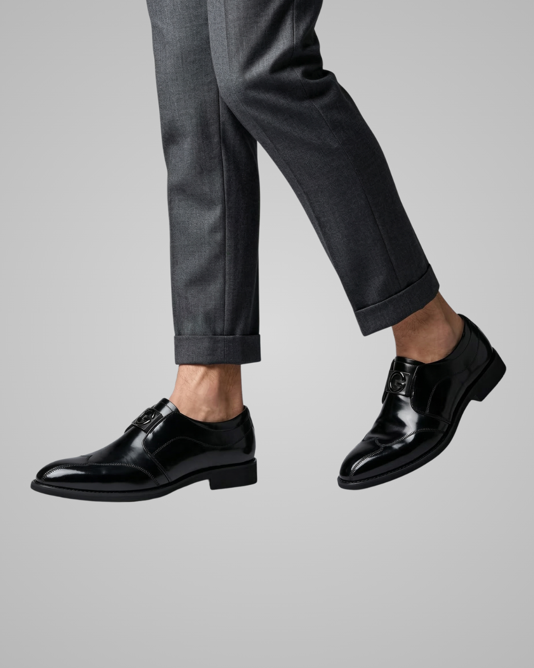 Black dress shoes worn with gray pants on a light gray background