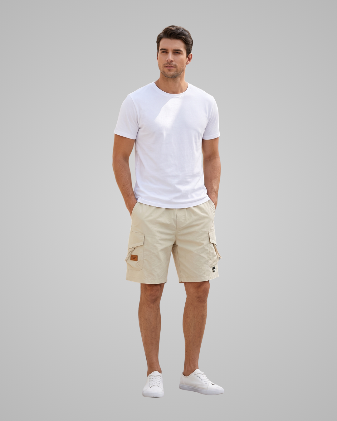 A man modeling a white crew-neck t-shirt and beige cargo shorts against a solid gray studio background.
