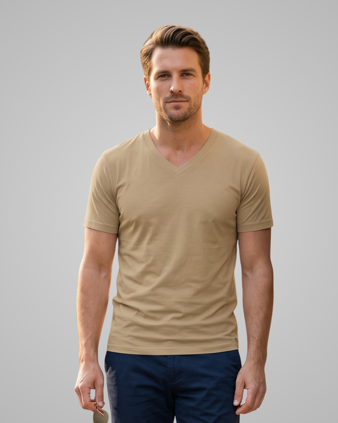A man wearing a beige v-neck t-shirt and navy blue pants, standing against a solid gray studio background.