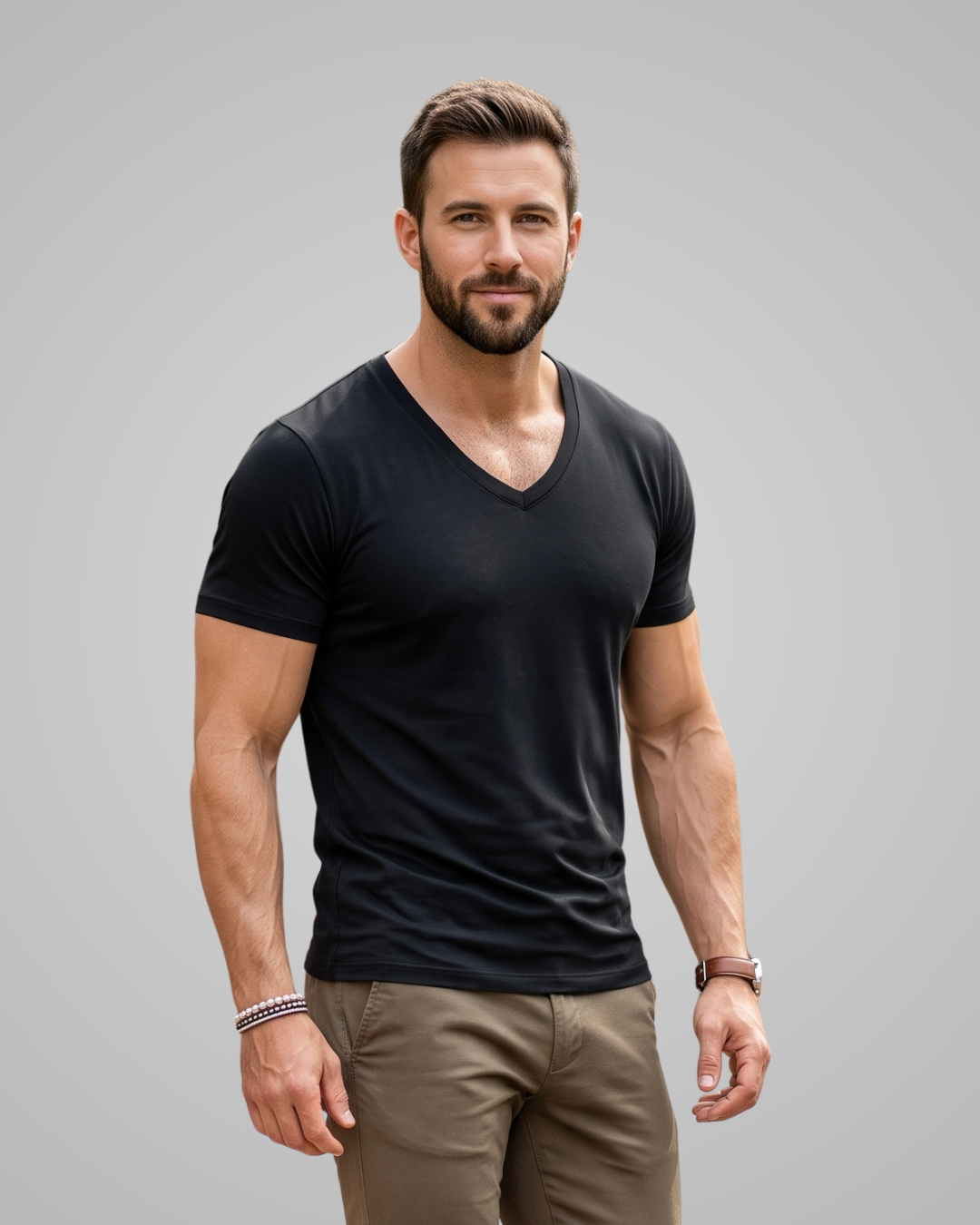 A muscular man with a beard modeling a black short-sleeve V-neck t-shirt and khaki pants against a solid gray studio background.
