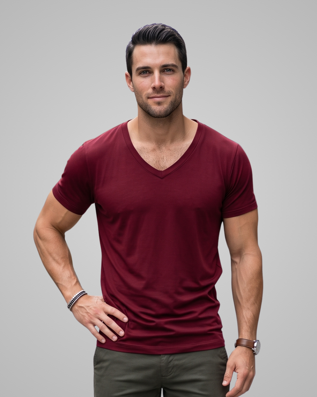 A man wearing a short-sleeve v-neck t-shirt in burgundy, paired with dark gray pants, standing against a solid gray studio background.