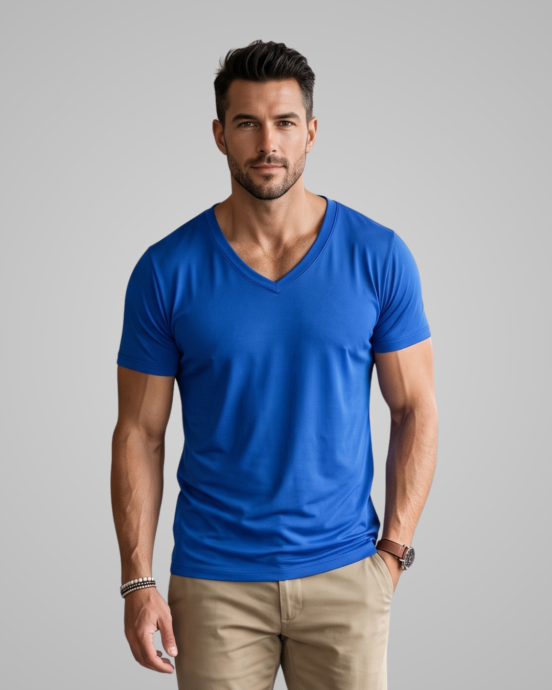 A man wearing a bright royal blue v-neck t-shirt and khaki pants, standing against a solid gray studio background.