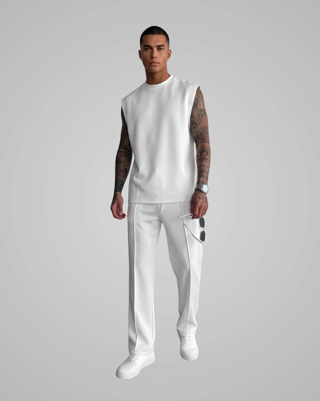 A man modeling a white sleeveless crewneck top and matching white pants against a solid gray studio background.