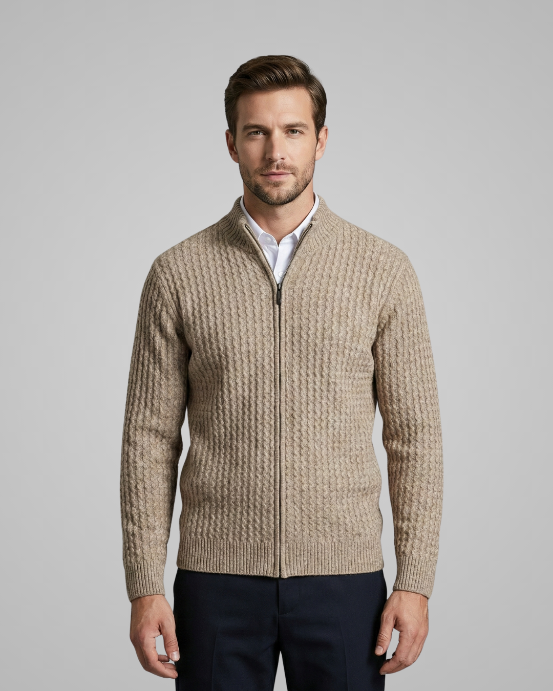 Man wearing a beige knit cardigan over a white shirt on a gray background