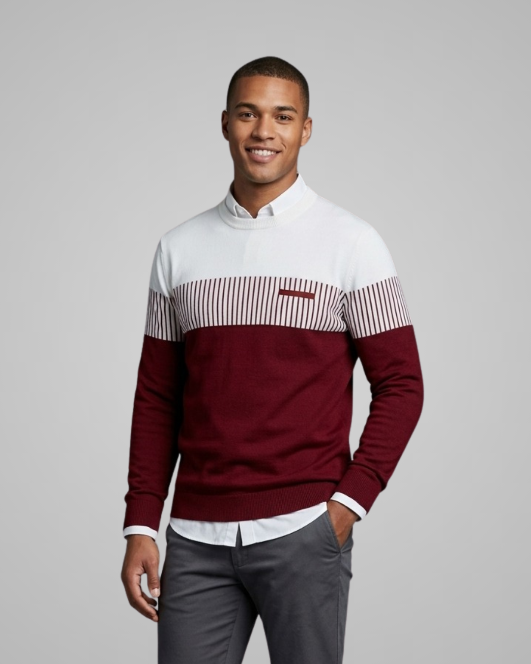 Man wearing a color-blocked sweater with a white shirt and gray pants on a gray background