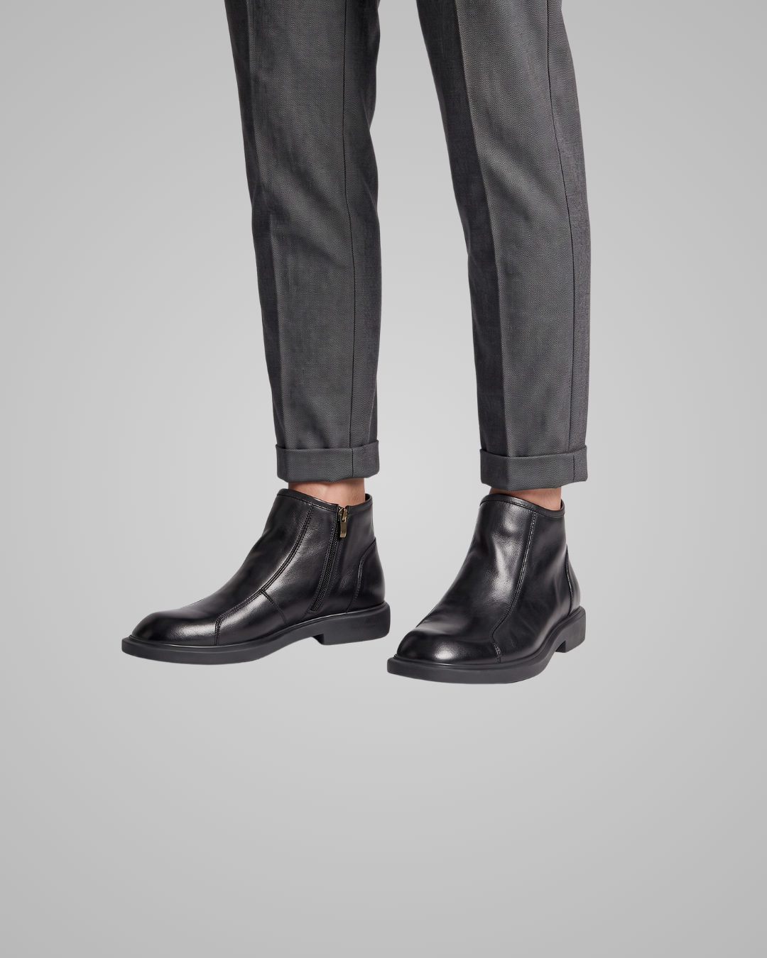 Black leather boots worn with gray pants on a light gray background