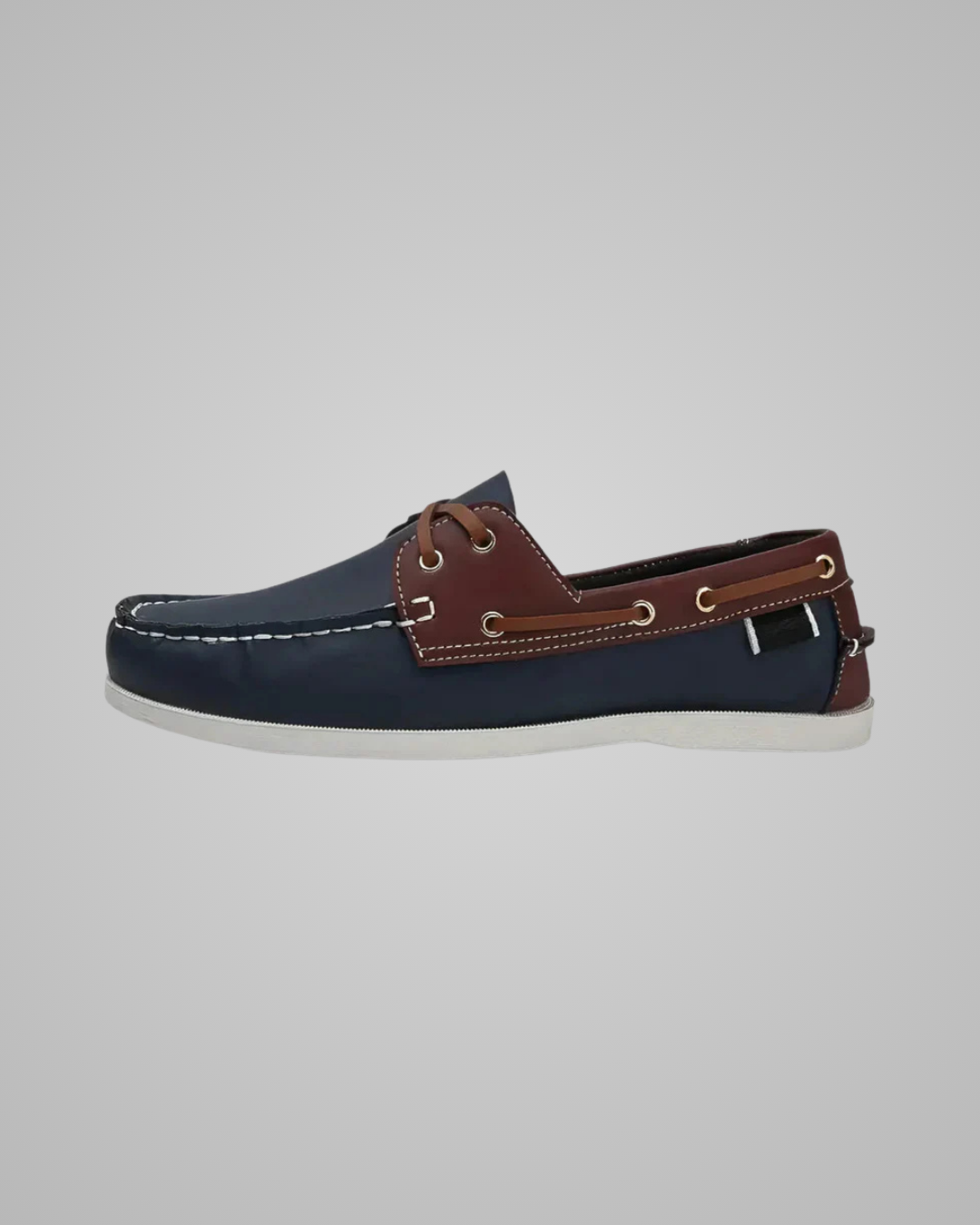 A single boat shoe in navy blue and brown leather with white stitching and a white sole, shown in profile against a light gray background.