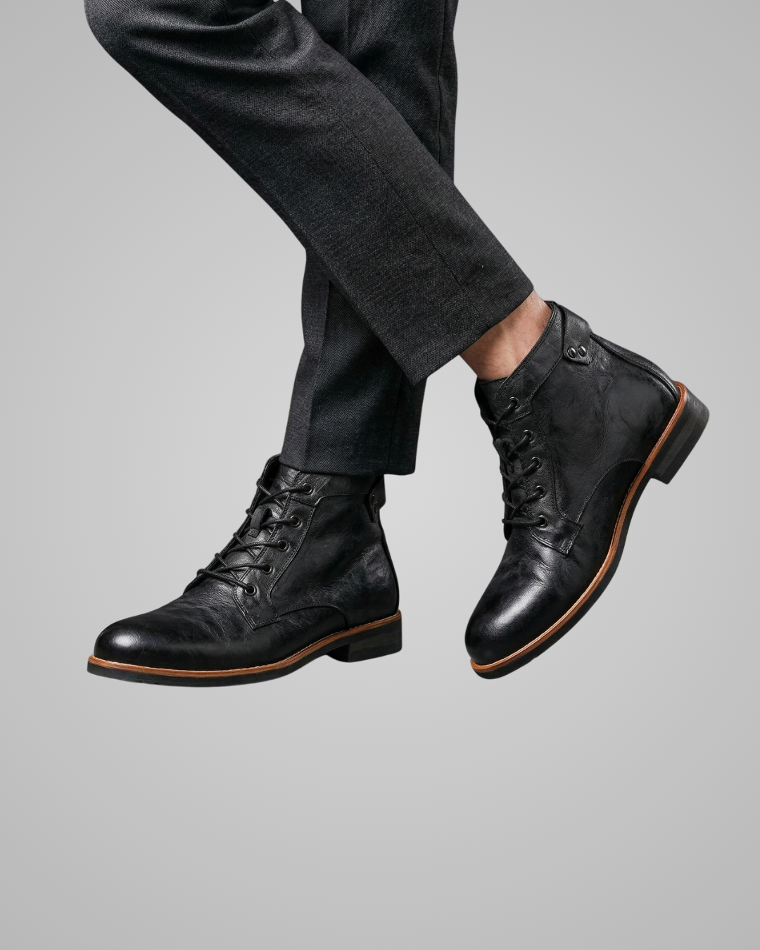 Black leather boots worn with gray pants on a light gray background