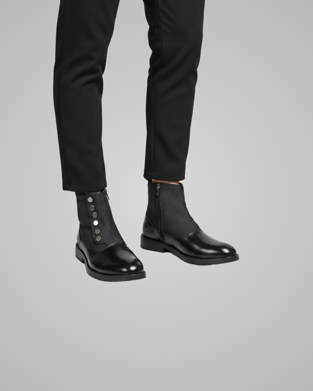 Black leather Chelsea boots worn with black pants on a gray background