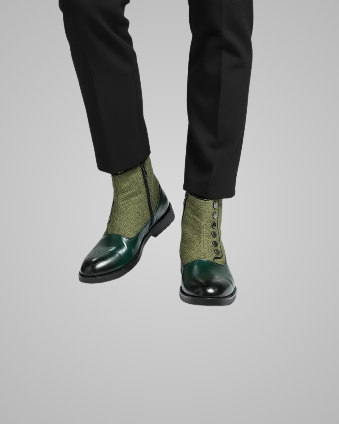 Green dress shoes with black soles worn with black pants on a light gray background