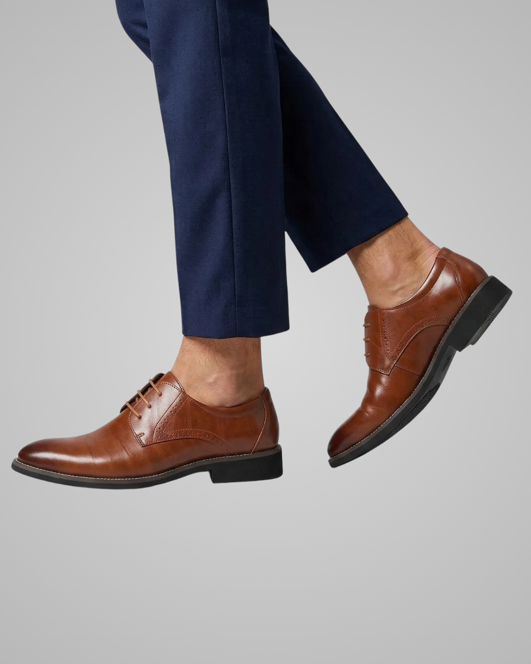 Brown dress shoes worn with navy pants on a gray background