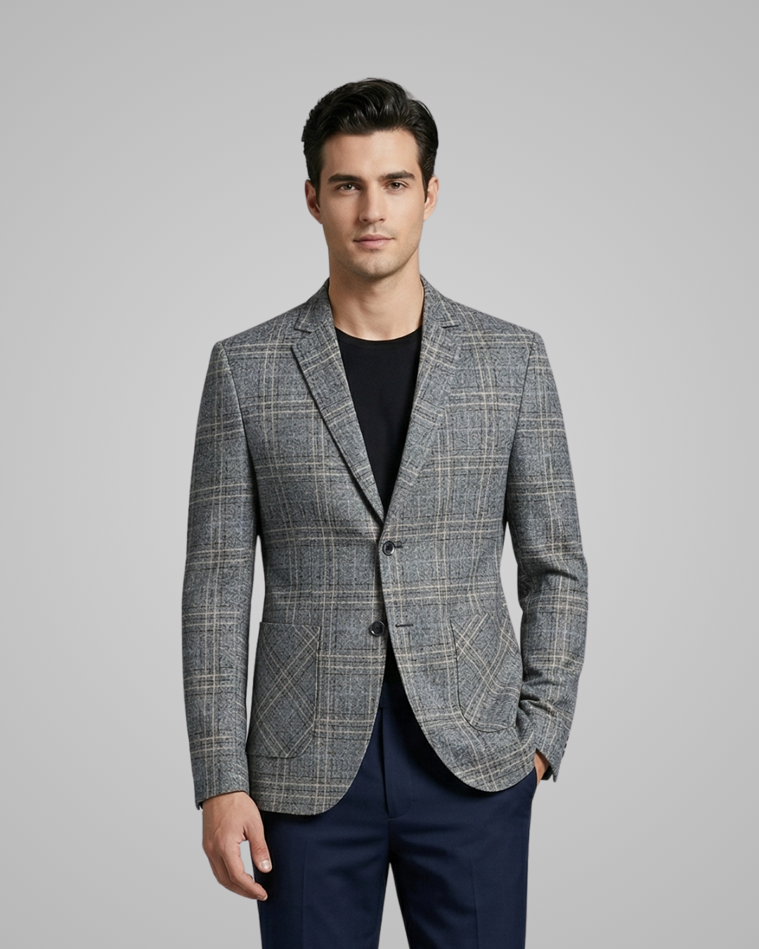 Man wearing a gray checkered blazer over a black shirt with navy pants on a gray background