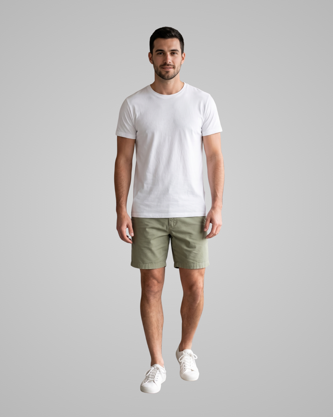 A man modeling a plain white short-sleeve crewneck t-shirt, olive green shorts, and white sneakers against a solid light gray background.
