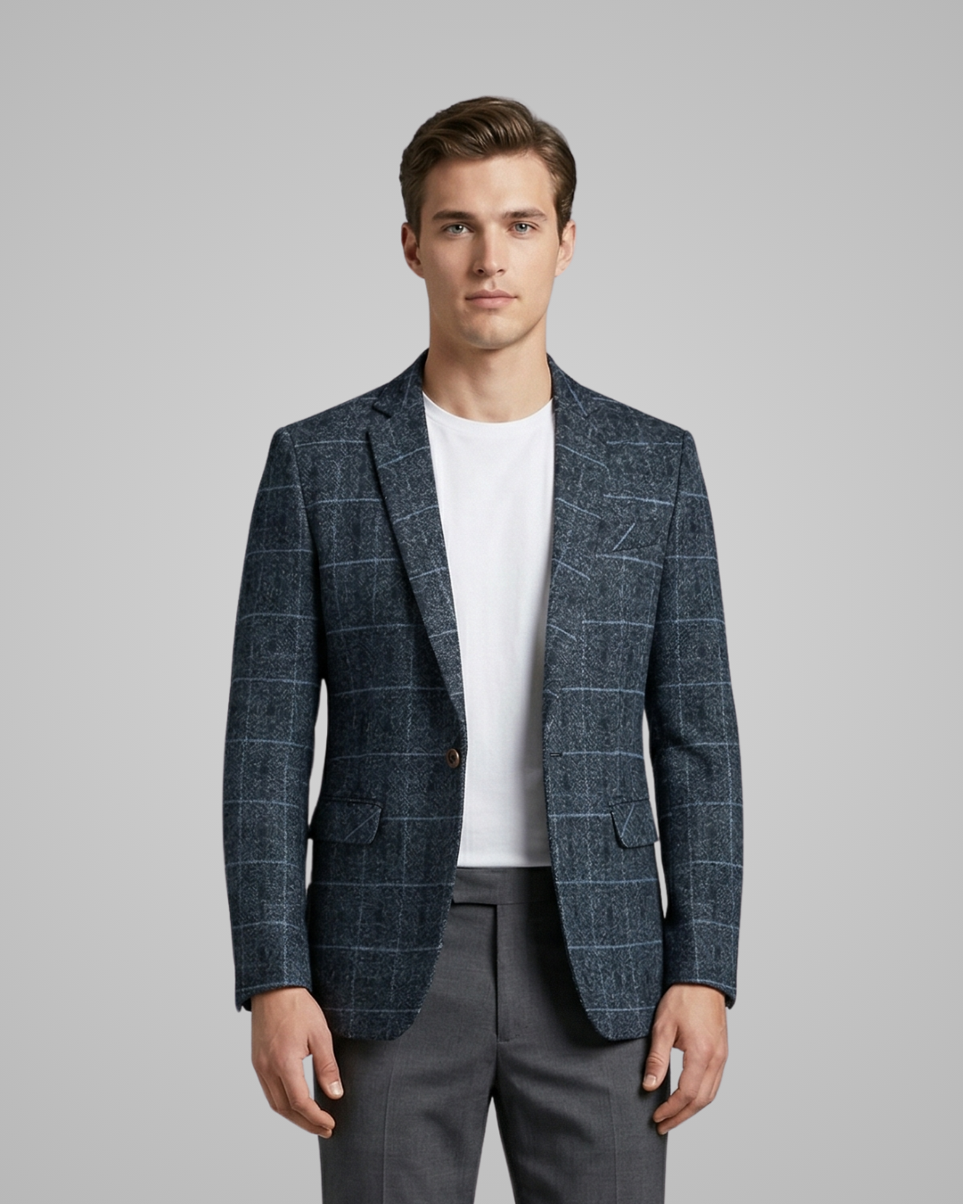 Man wearing a blue checkered blazer over a white shirt and gray pants on a gray background