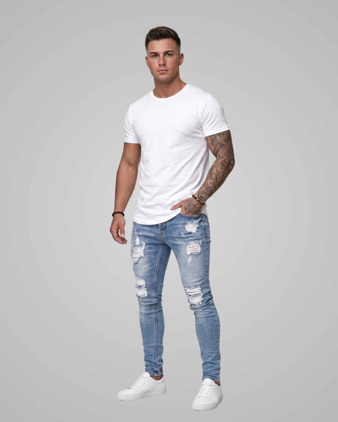Man wearing a white t-shirt and blue ripped jeans on a gray background