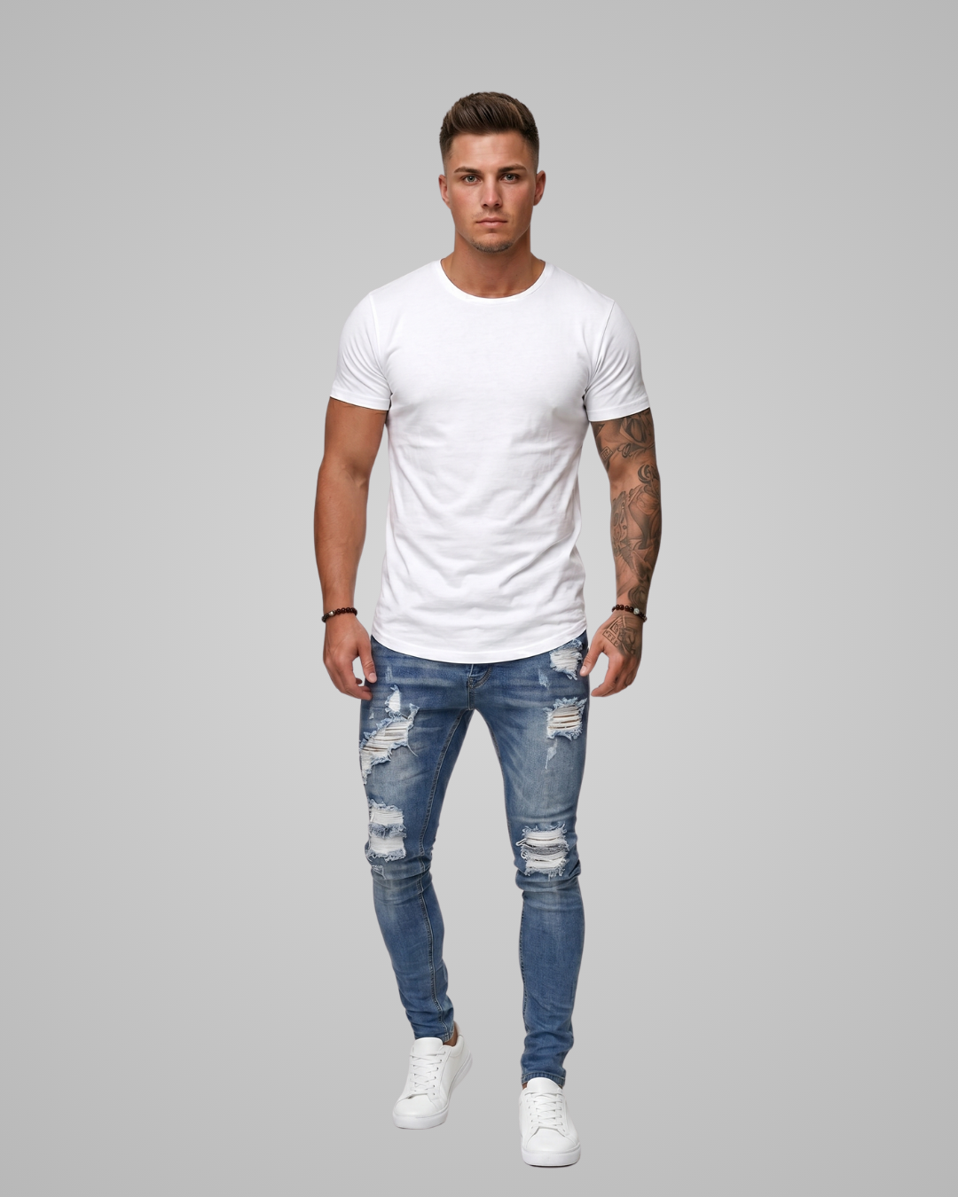 Man wearing a white t-shirt and blue ripped jeans on a gray background