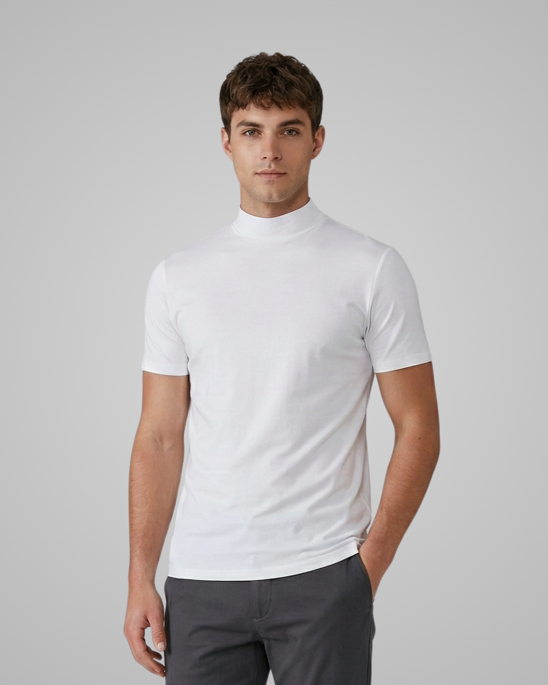 Man wearing a white turtleneck shirt and dark pants on a gray background