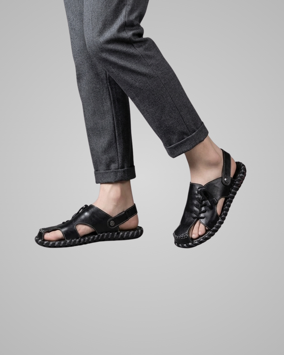 Black sandals worn with gray pants on a plain background