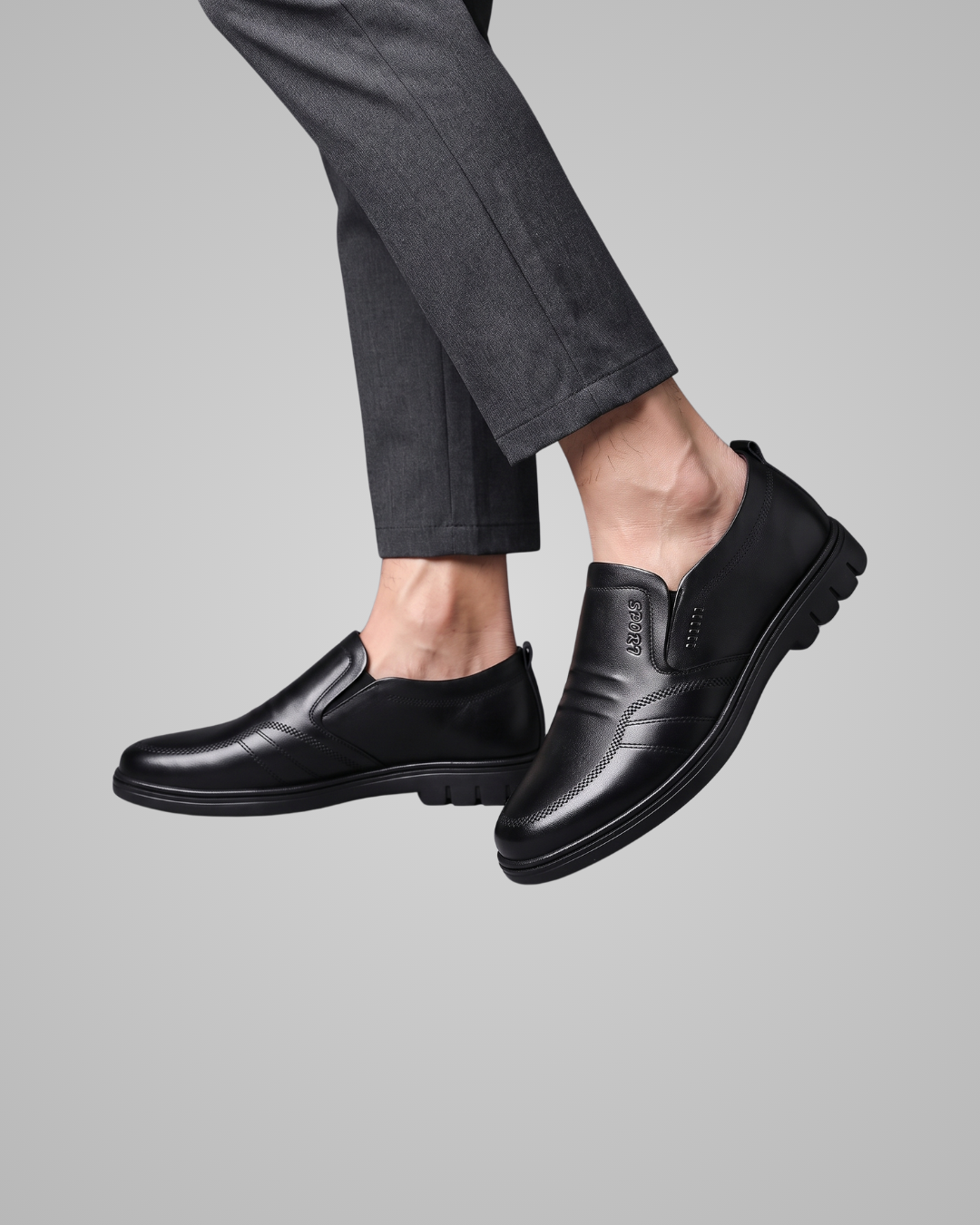 A pair of men's black leather slip-on loafers shown on a model's feet, paired with dark gray trousers, against a solid gray background.