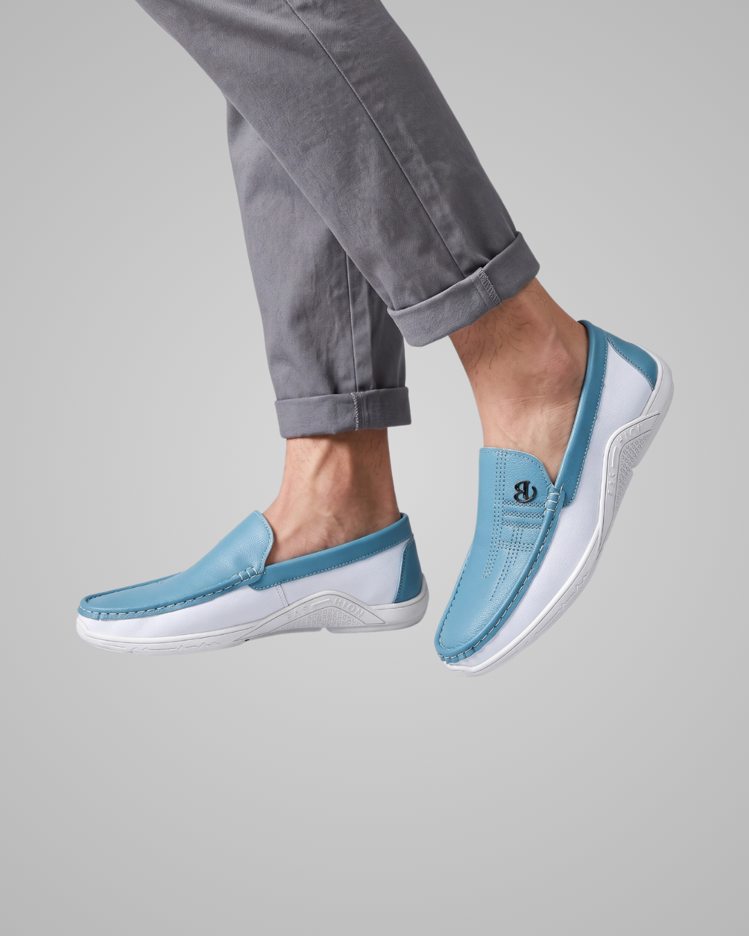 A person wearing light blue and white slip-on loafers with gray cuffed jeans, shown against a plain light gray studio background.