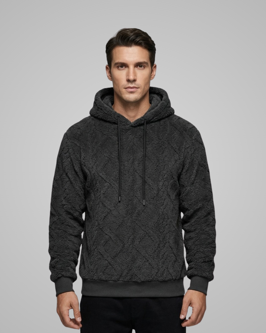 Man wearing a dark gray cable knit hoodie on a gray background