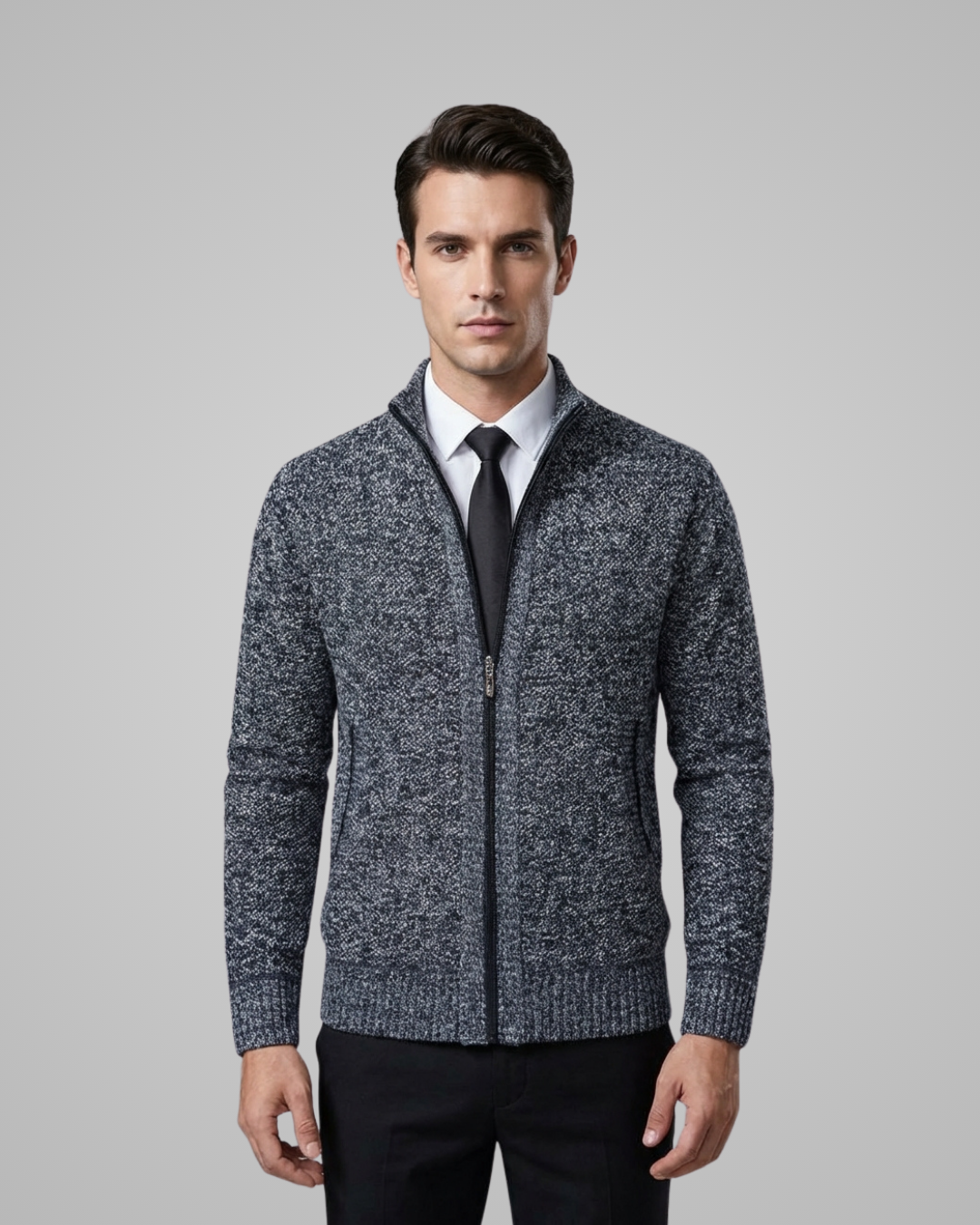 Man wearing a gray zip-up sweater over a white shirt with a black tie on a gray background