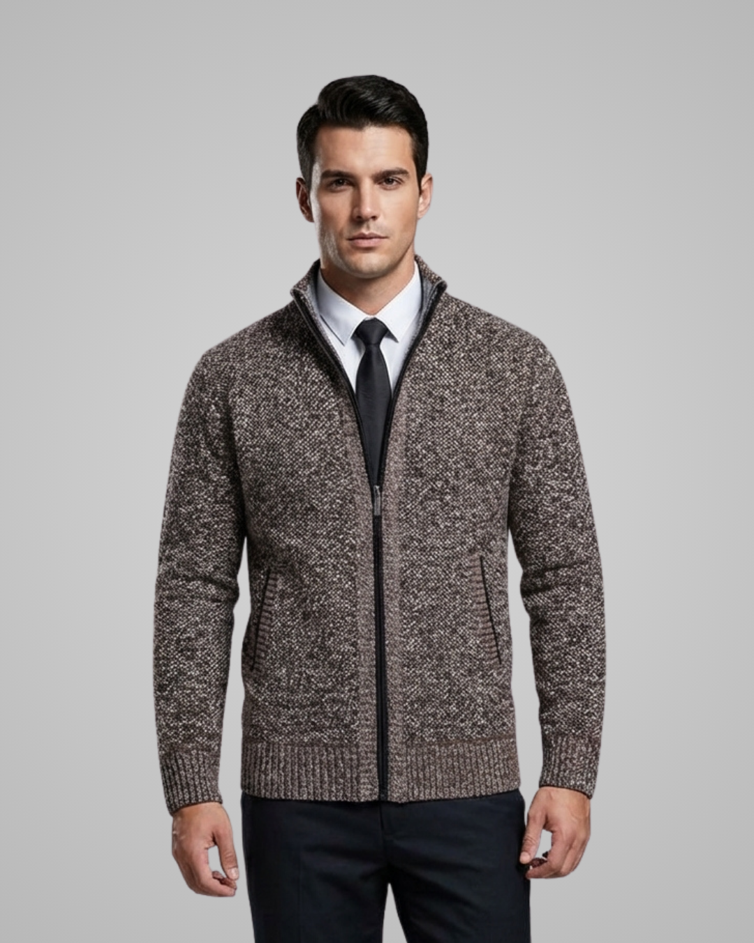 Man wearing a brown zip-up sweater over a white shirt with a black tie against a gray background