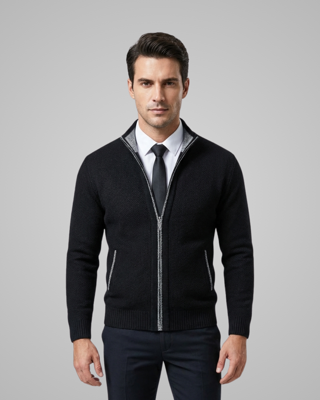 Man wearing a black zip-up sweater over a white shirt with a tie on a gray background