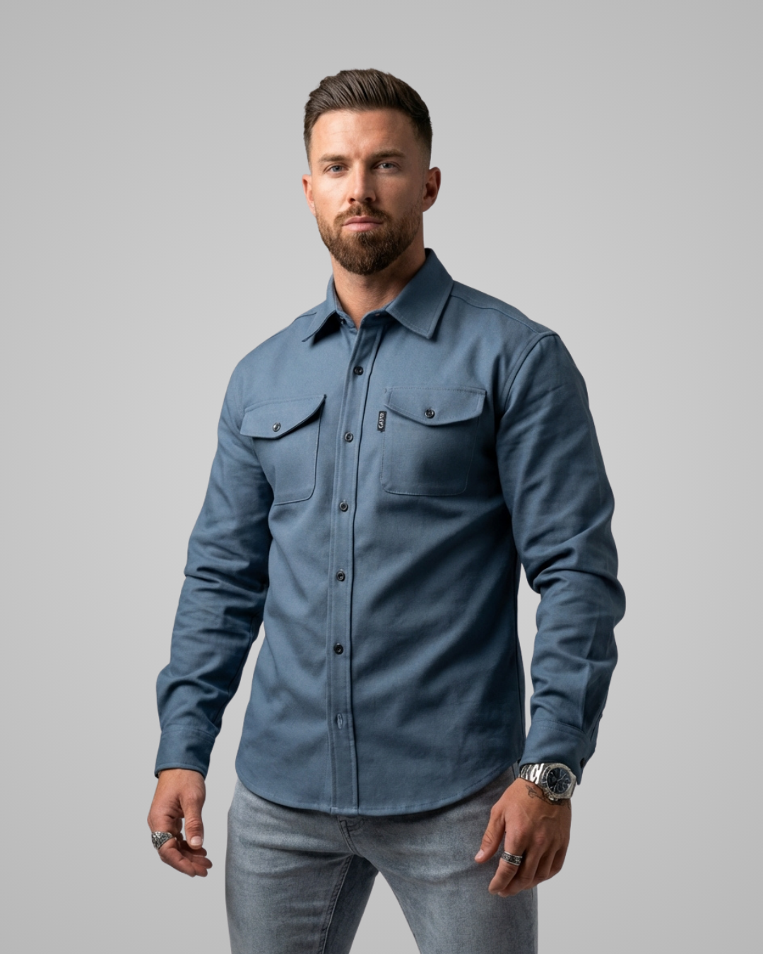 Man wearing a blue button-up shirt and gray pants against a gray background