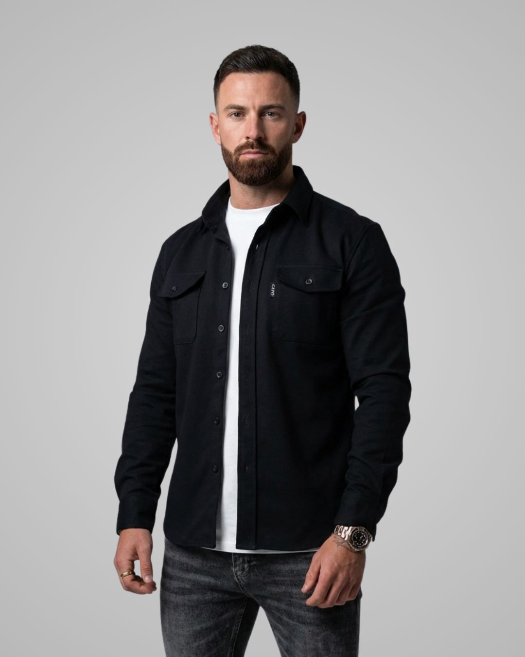 Man wearing a black jacket over a white shirt on a gray background