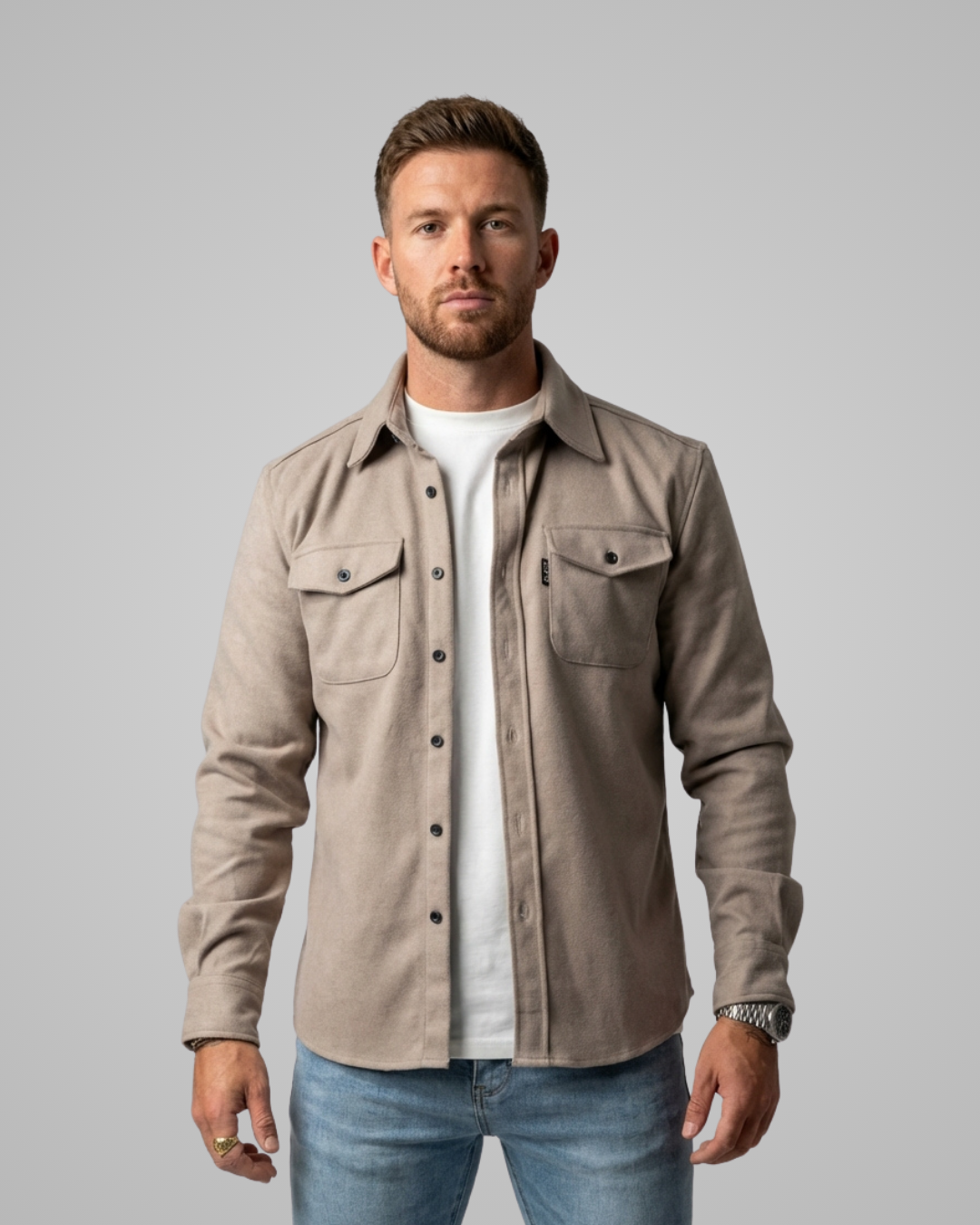 Man wearing a beige button-up shirt over a white t-shirt on a gray background
