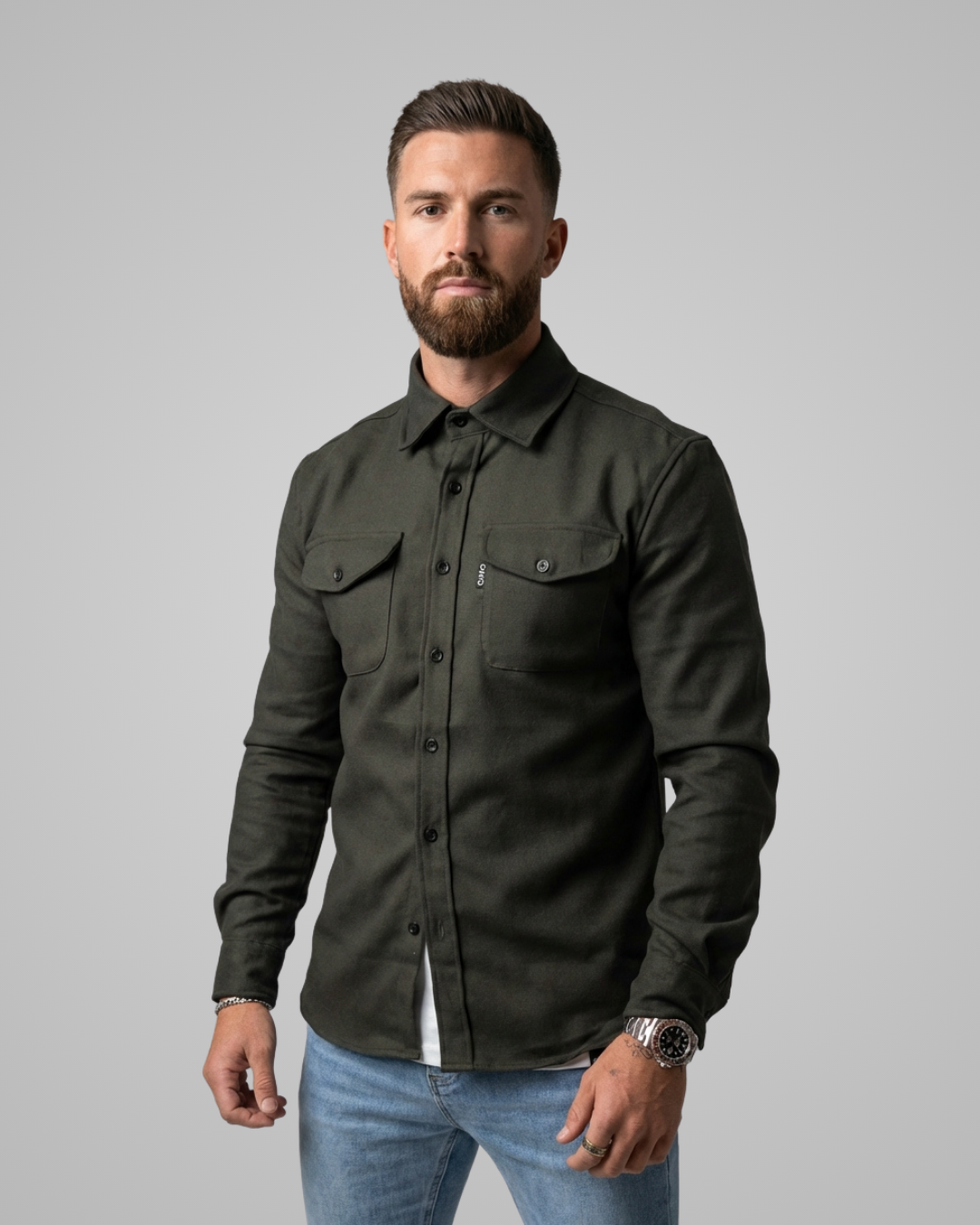 Man wearing a dark green shirt and blue jeans against a gray background