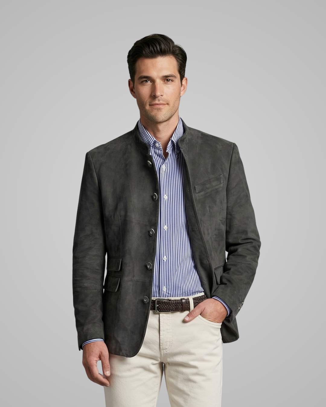 Man wearing a dark gray blazer over a striped shirt with light-colored pants on a gray background
