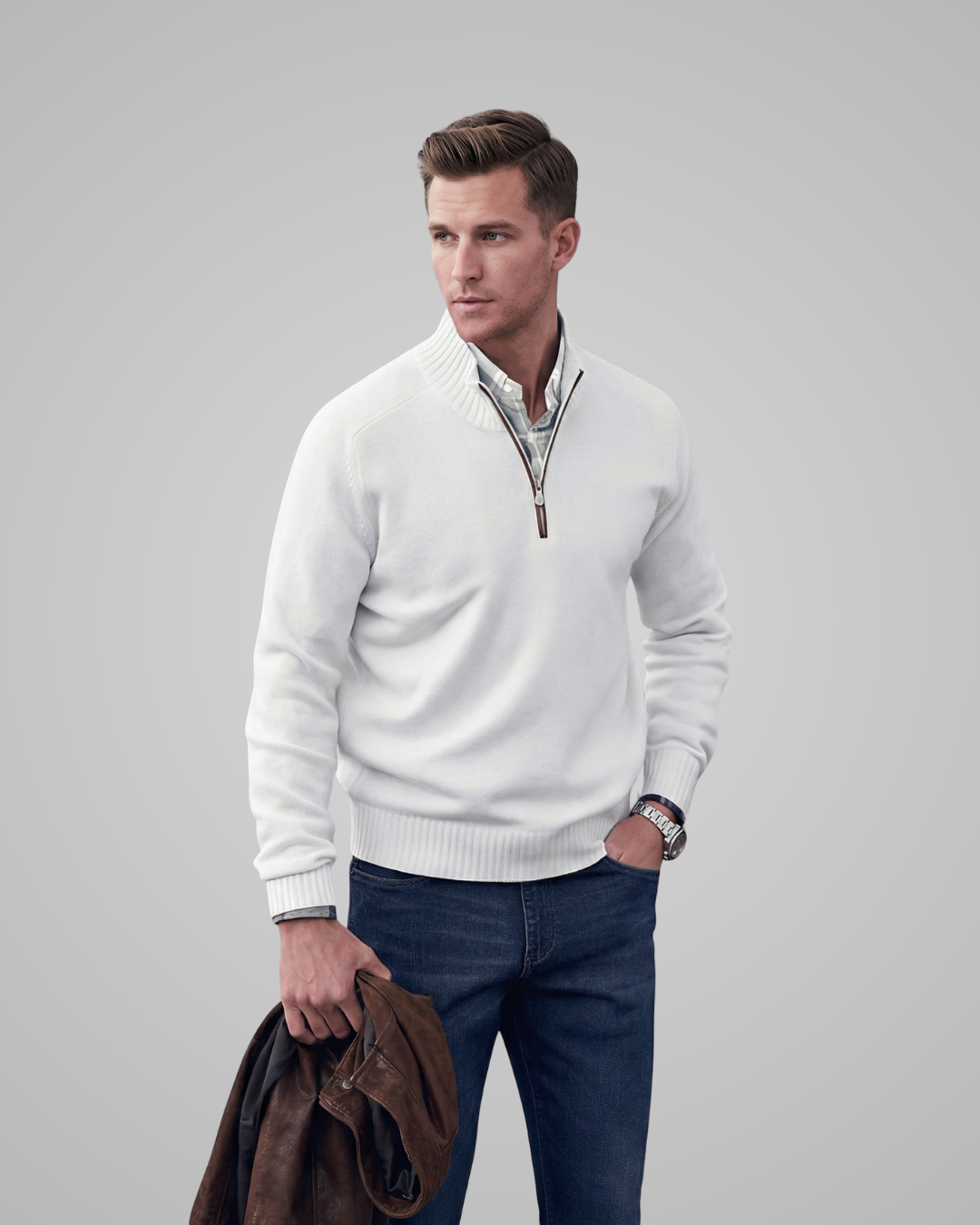 Man wearing a white sweater with a zipper, holding a jacket against a gray background