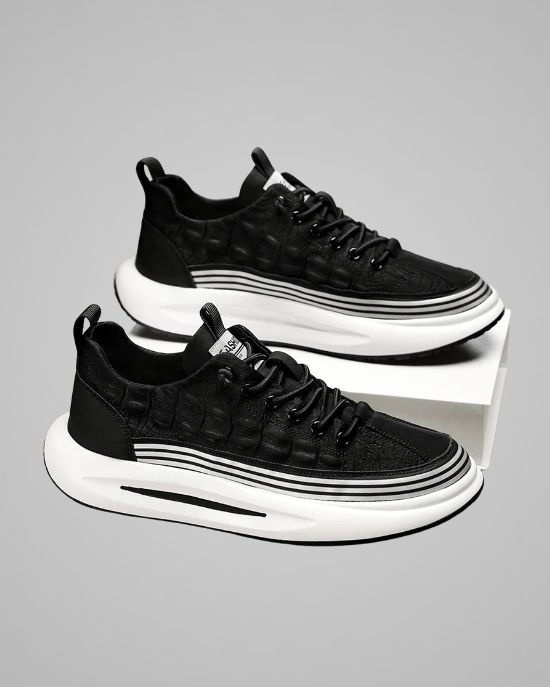 Black sneakers with white soles on a reflective surface against a gray background