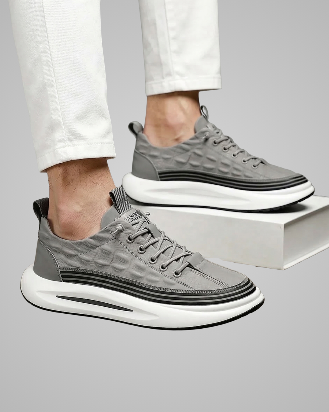 Gray sneakers with a white sole worn by a person on a gray background