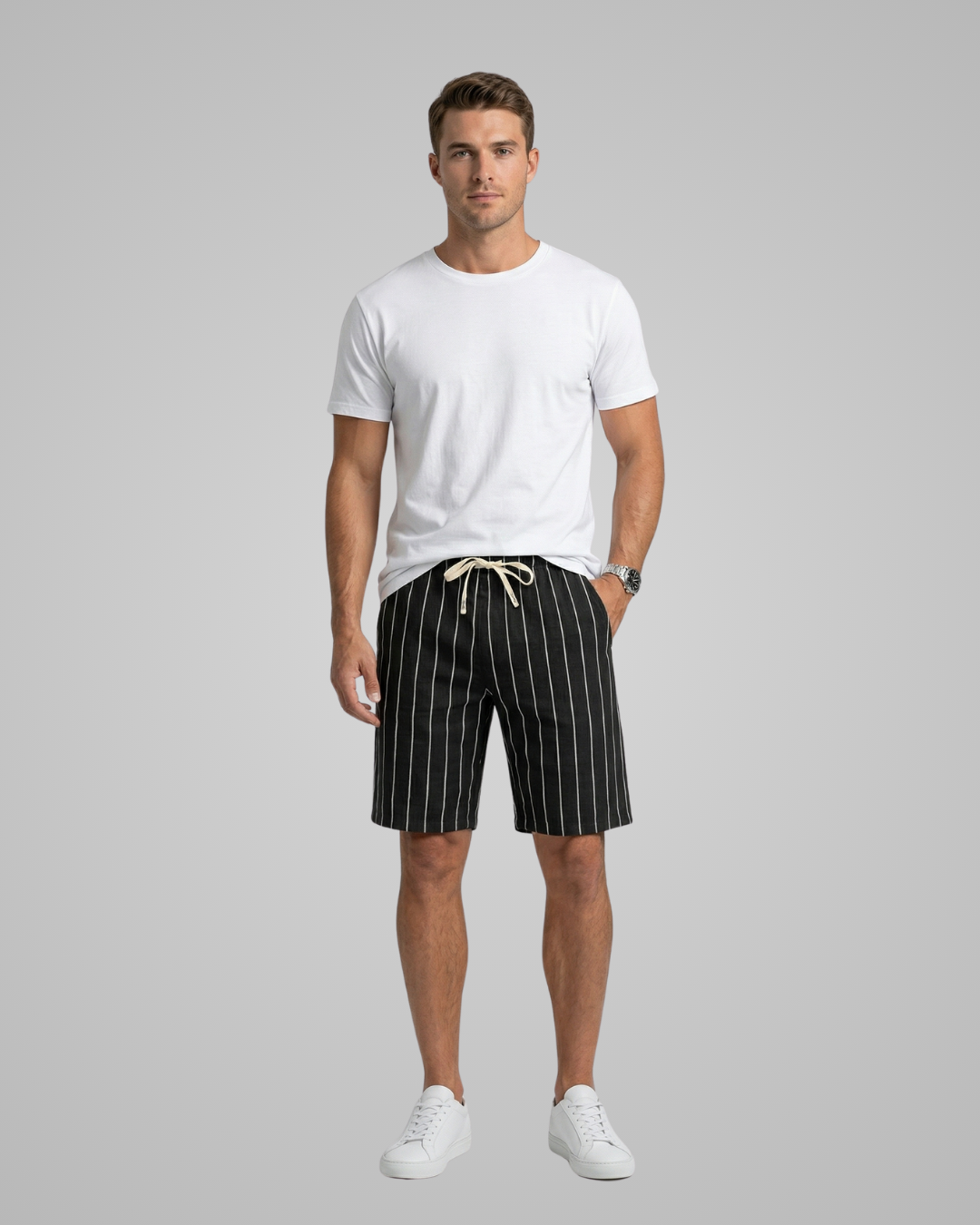 Man wearing a white t-shirt and black striped shorts on a gray background