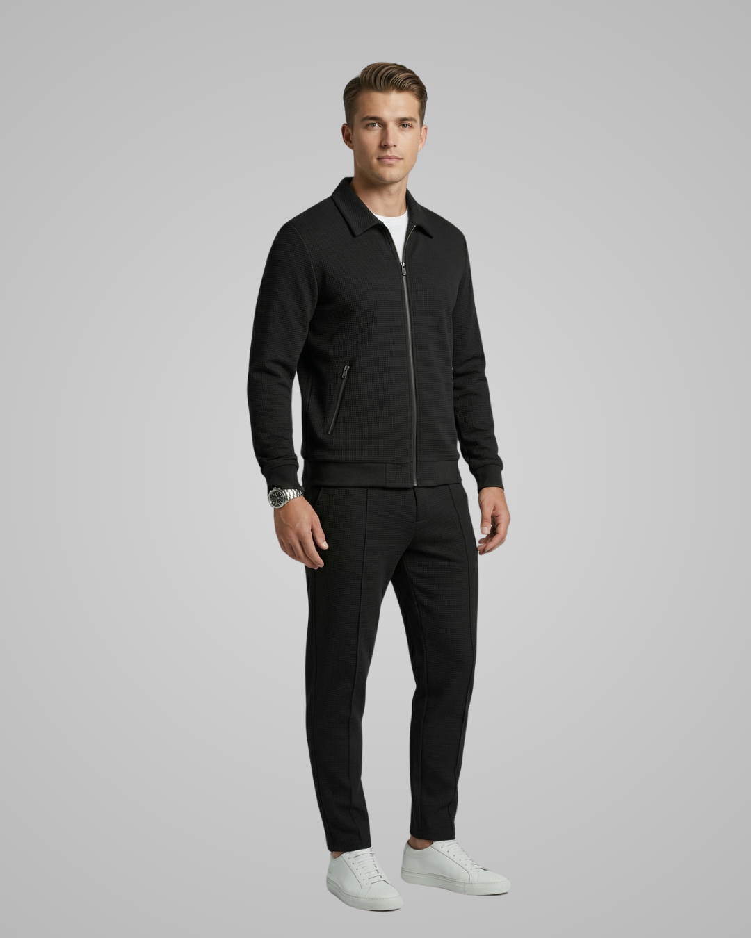 Man wearing a black jacket and pants with white shoes on a gray background