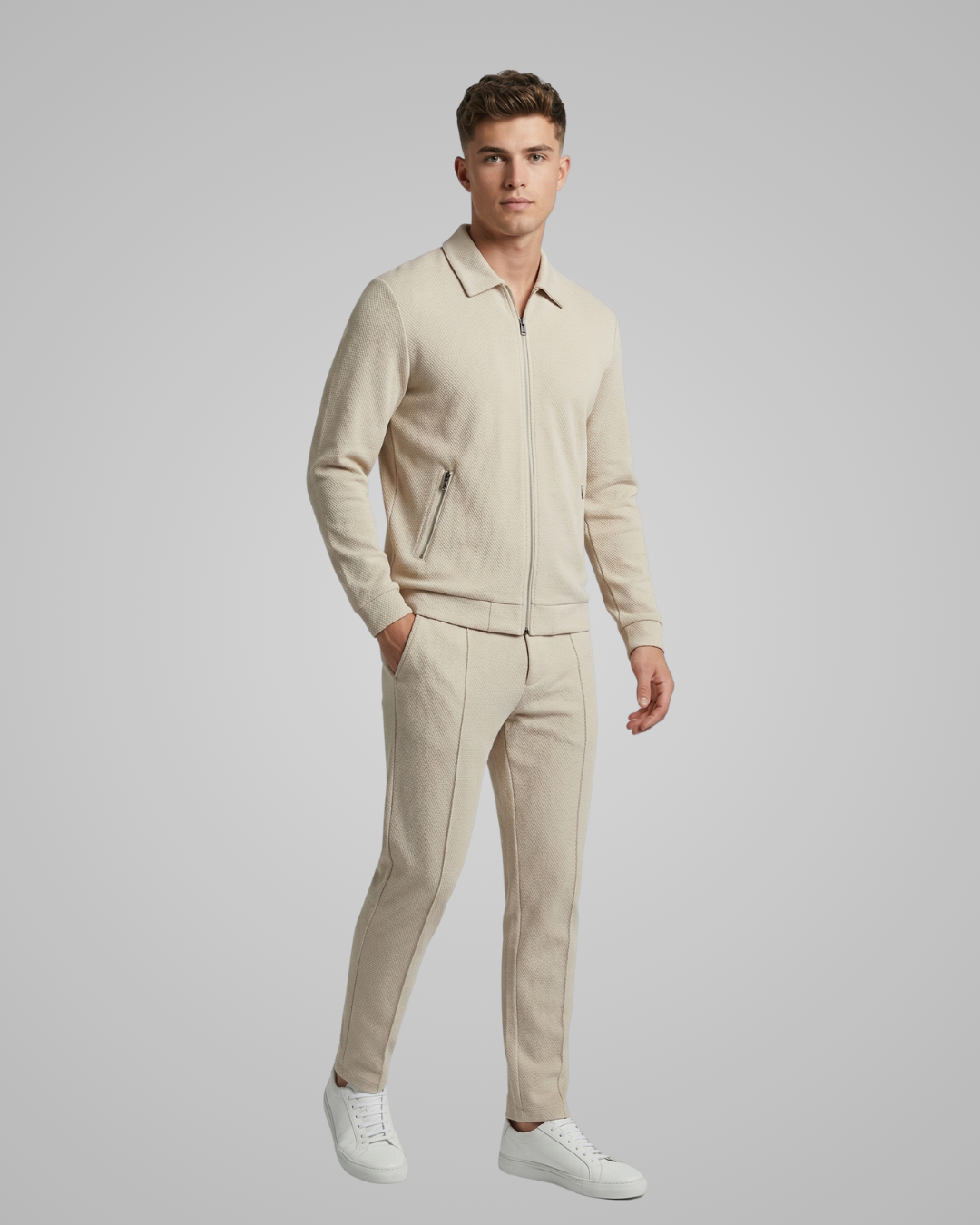 Man wearing a beige outfit with a matching jacket and pants on a gray background
