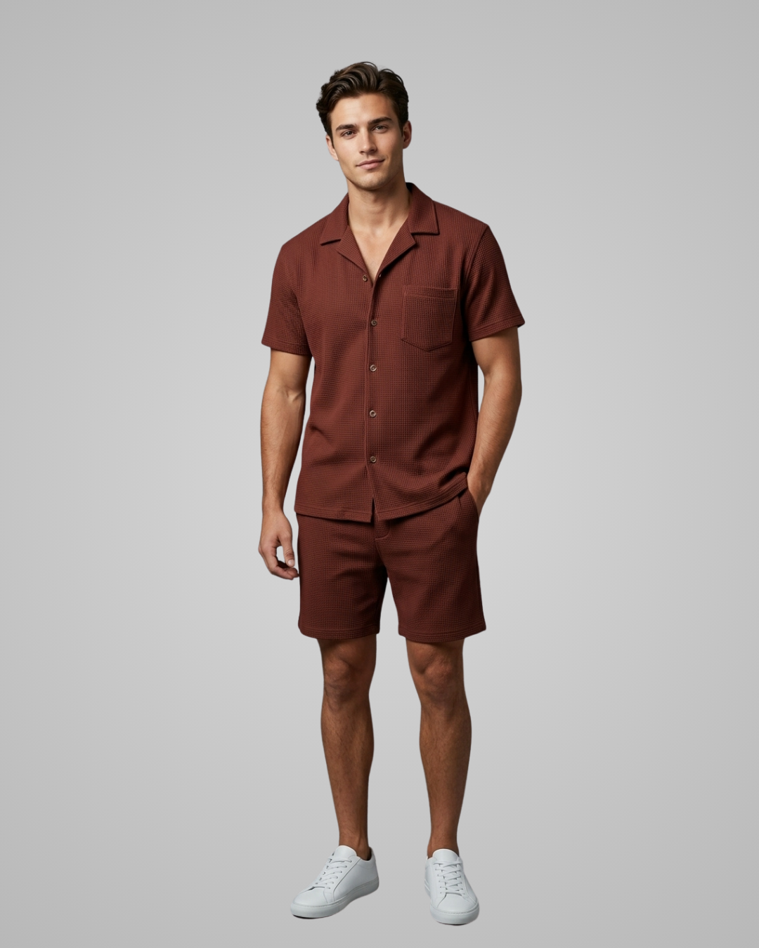 Man wearing a brown shirt and shorts set with white sneakers on a gray background
