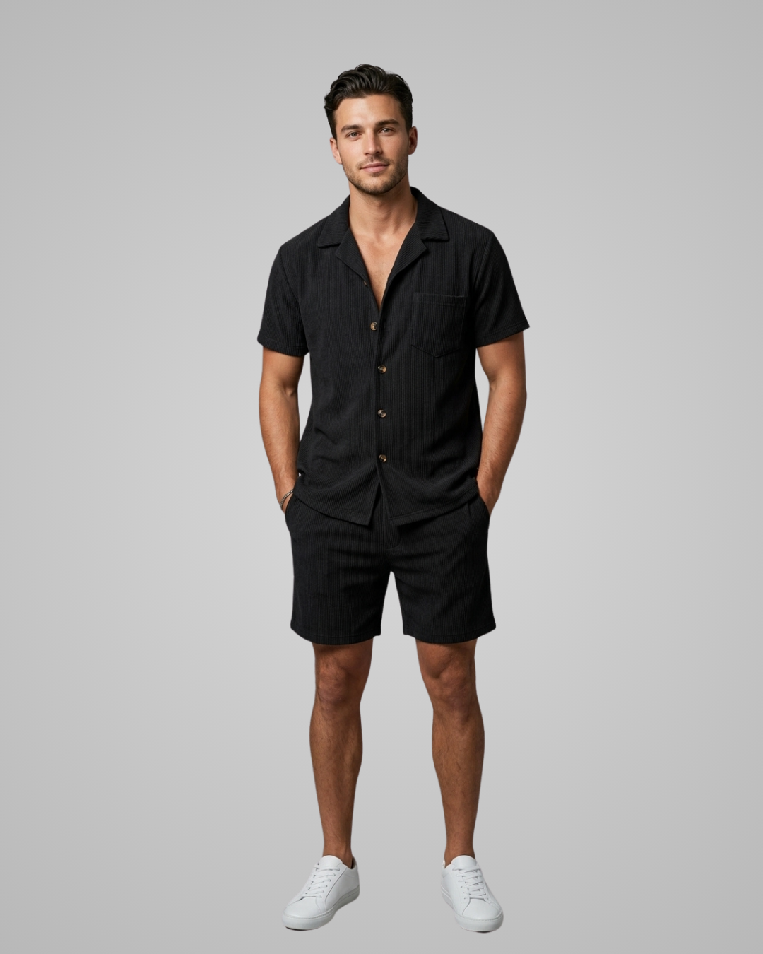 Man wearing a black shirt and shorts set with white sneakers on a gray background
