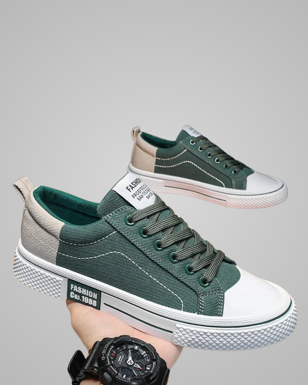 Green and gray sneakers with white soles held by a hand wearing a black watch on a gray background