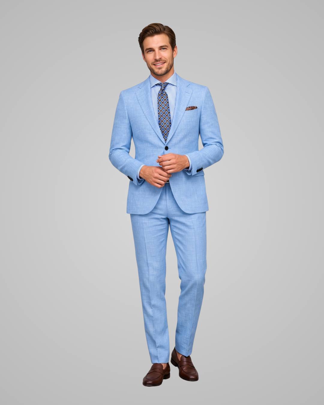 A man modeling a light blue two-piece suit with a patterned blue and white tie, a brown pocket square, and brown dress shoes, set against a solid gray studio background.