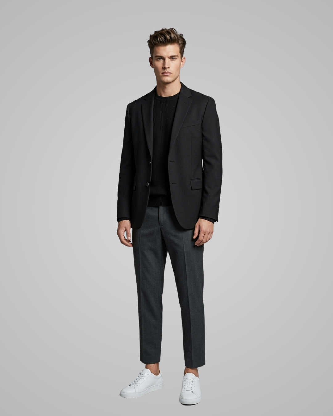 Man wearing a black blazer and gray pants with white sneakers on a gray background
